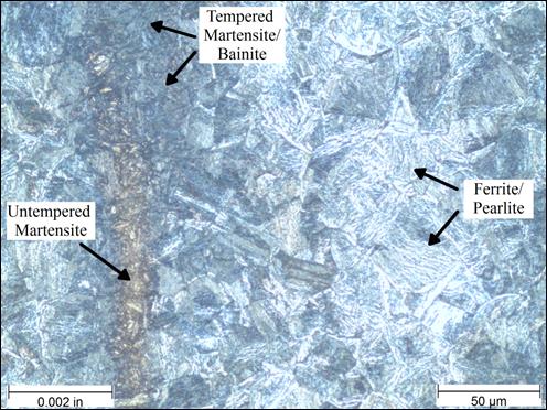 Figure 31. Photo. Micrograph near rod core etched with 10-percent potassium metabisulfite at 500x magnification. This photo shows a micrograph that was taken near the core of the threaded rod at a magnification of 500x and viewed under polarized light. The sample was etched with 10‑percent potassium metabisulfite. A scale bar with a length of 0.002 inches is shown in the lower left corner of the photo, and a scale bar with a length of 50 micrometers is shown in the lower right corner. The microstructure has a few distinct features. There is a vertical band of dark blue needle-like tempered martensite and bainite microstructures near the left-center of the micrograph. Just to the left of that is a thin vertical band of gray needle-like untempered martensite. The right half of the photo consists mainly of less dense lighter blue ferrite and pearlite. The ferrite exists appears similar to fish scales, and the pearlite appears as patches of parallel lines