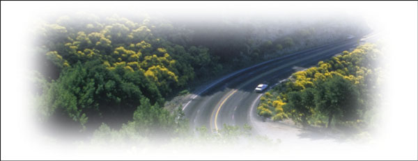 Overhead view of a curving four-lane rural road with trees on both sides.