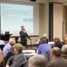 Speaker standing in front of projector screen with people sitting at tables