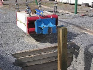 The figure shows a rectangular pendulum swinging mass representative of the weight of a 4,400 pound pickup truck. It is constructed of reinforced concrete and steel suspended by metal hooks and chains.