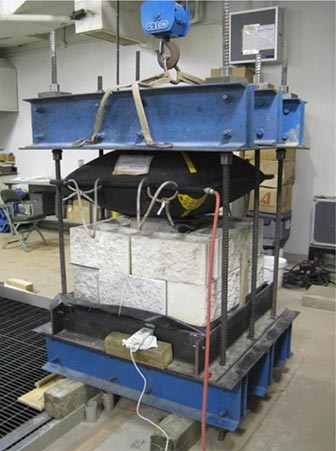 This is a photo showing a calibration reaction assembly with two courses of concrete masonry blocks stacked up and an inflated airbag pressed against them from the top.