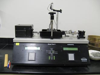 This is a photo showing a front view of a standard direct shear device. There are controllers on the bottom with the shear box on the top, connected to a motor and a load cell.