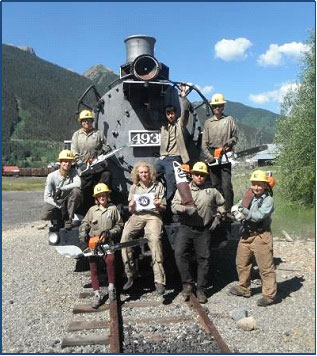 Photo of a group of people posing for a picture in front of a engine train.