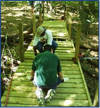 Photo of 2 people working on building a wooden trail bridge.