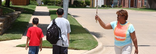 image of a crossing guard holding a stop sign for two kids to cross