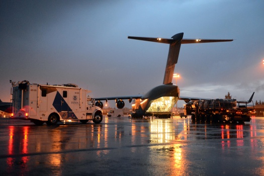 A white mobile emergency response vehicle waits to be loaded into a large aircraft.