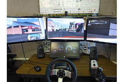 This image shows a desktop simulator located  inside the Mobile Sign Laboratory. The driving display consists of three computer  desktop monitors that show a driver’s view while a fourth, smaller screen, replicates an instrument cluster.