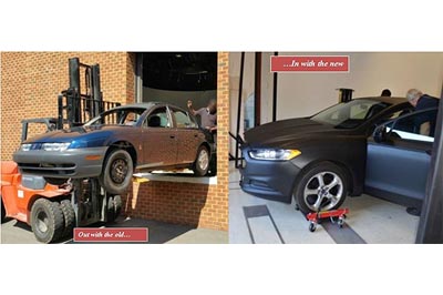 This image shows an old sedan being removed from a large laboratory door and a newer sedan inside the laboratory. The new vehicle will replace the old vehicle in the Highway Driving Simulator.