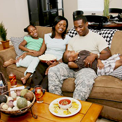 Service member sitting on a couch with his son lying across his lap, his wife next to him and his daughter