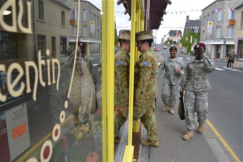 Australian Capt. Mel Ross, 41, of Nowra, New South Wales, an officer attached to the British 4th Parachute Regiment and U.S. Army paratroopers shop for souvenirs along Rue du Général de Gaulle in Sainte-Mère-Eglise, France. 
