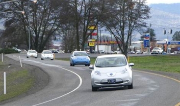 Photo of an S curve in a road with 4 cars and a gas station in the background.