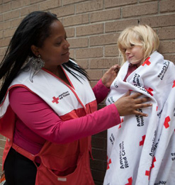 Red Cross Volunteer helps little girl wrapped in Red Cross blanket