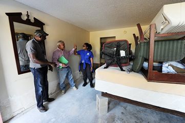 'Hazard Mitigation Specialist Francis (left) and FEMA Corps member Celcia (right) celebrate with business owner Satpal about the steps he took to mitigate the flood effects from Hurricane Matthew. Satpal and his staff elevated the beds on cinder blocks which saved the contents from flood waters. (Photo by Jocelyn Augustino/FEMA)'