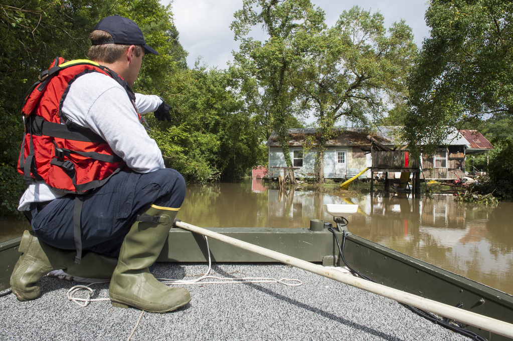 Man on boat pointing towards flooded house.