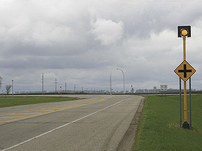 In Minnesota, Mn/DOT has removed overhead beacons at about 30 intersections, instead placing the yellow beacons on the ground-mounted signing for mainline traffic. A yellow beacon is shown here affixed above a sign alerting motorists that an intersection is ahead. Credit: Mn/DOT