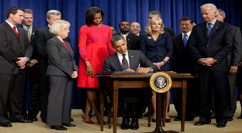 Picture of Obama signing papers with Michelle Obama and the White House staff 