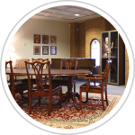 table with chairs, piano, glass cases, and pictures hanging on the wall 