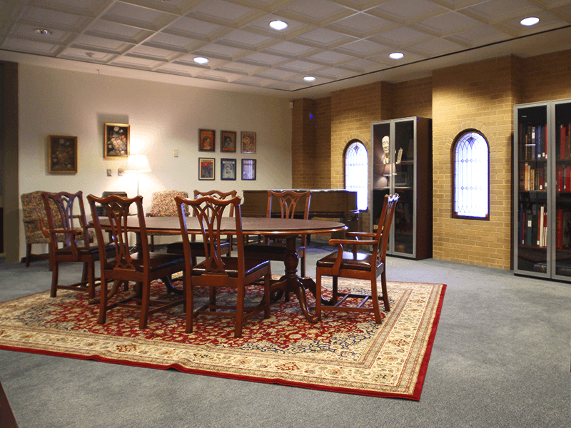 table with chairs, piano, glass cases, and pictures hanging on the wall 