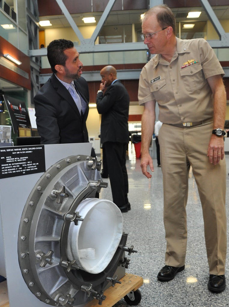 WASHINGTON - Naval Surface Warfare Center Dahlgren Division (NSWCDD) engineer Helmer Flores demonstrates how a shipboard Collective Protection System (CPS) filter housing works while briefing Rear Adm. Brian Antonio, program executive officer for the Littoral Combat Ships program, on the system and its capabilities during the NSWCDD Briefing and Technical Demonstration held at Naval Sea System Command headquarters, Nov. 3. NSWCDD chemical, biological and radiological (CBR) defense engineers designed the shipboard collective protection system to protect Sailors, critical operations, and equipment within selected areas of a ship, or zones, from CBR contamination when the ship is operating in a contaminated environment. Personnel in the protected zone do not need to wear protective clothing or masks which impose heat stress and can impact crew members' performance.  