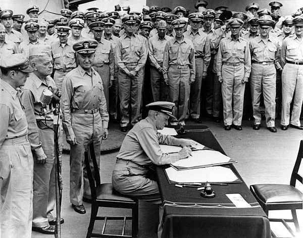 Photo #: 80-G-701293 Surrender of Japan, Tokyo Bay, 2 September 1945 Fleet Admiral Chester W. Nimitz, USN, signs the Instrument of Surrender as United States Representative, aboard USS Missouri (BB-63), 2 September 1945. Standing directly behind him are (left-to-right): General of the Army Douglas MacArthur; Admiral William F. Halsey, USN, and Rear Admiral Forrest Sherman, USN. U.S. Navy photo