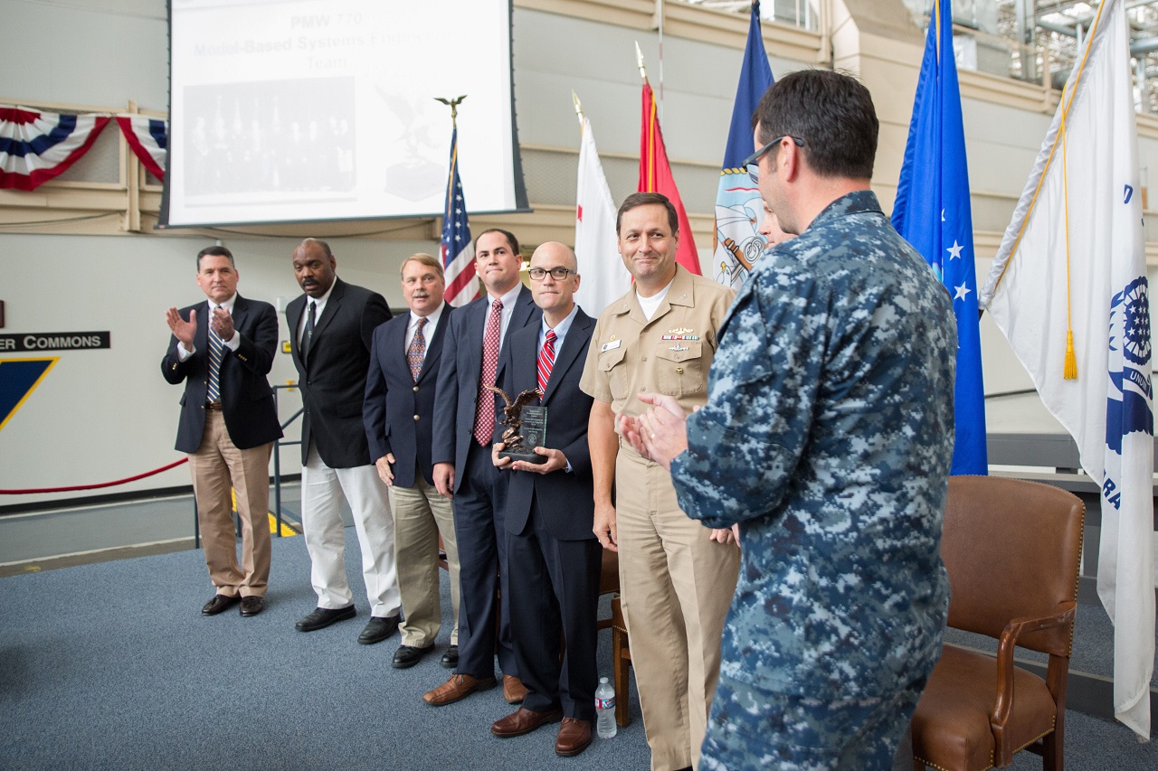 SAN DIEGO (Nov. 28, 2016) The Navy’s Undersea Integration Program Office (PMW 770) Model Based Systems Engineering (MBSE) team receives applause from Rear Adm. Christian "Boris" Becker, right, commander, Program Executive Office for Command, Control, Communication, Computers and Intelligence (PEO C4I) and Mr. John Pope III, executive director PEO C4I, left, for receiving the Department of the Navy 2016 Innovation Excellence Acquisition Team of the Year award. The team was initially presented the award during an awards ceremony at the Pentagon Nov. 17, 2016. PMW 770 uses MBSE to quickly integrate commercial off-the shelf technology and modernize the Navy’s current technologies to work with already existing systems.  Navy photo by Krishna M. Jackson/Released