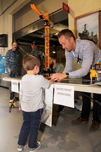 NORFOLK, Va. (April 21, 2016) - Mid-Atlantic Regional Maintenance Center (MARMC) Waterfront Operations Class Team Lead (Dock Landing Ships) Chris Dellinger assists a student in remotely moving a model ship antenna, by toy crane, onto a Lego replica destroyer during MARMC's Two hundred students from three area middle schools, Deep Creek, Great Bridge and Crestwood, visited MARMC to participate in the large STEAM Fair.