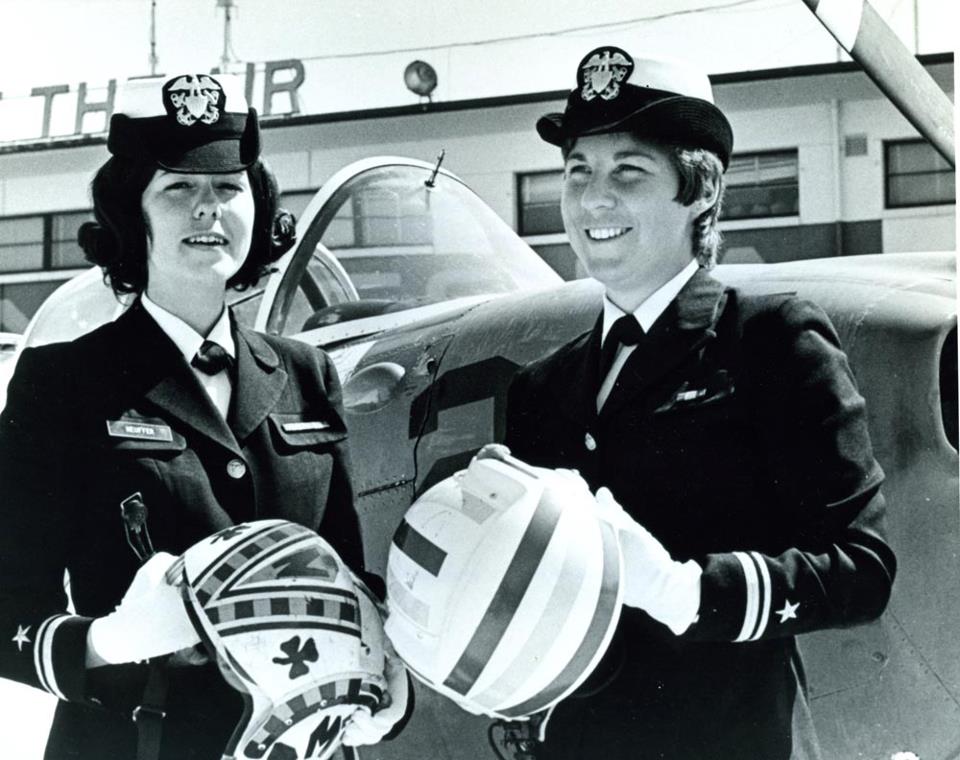 Lieutenants Junior Grade Judith A. Neuffer, left, and Barbara A. Allen get the feel of helmets they will be wearing during early flight training in the T-34 mentor trainer aircraft in the background. These women are two of the first four women officers to be chosen to undergo aviation training, March 1973. NHHC Photograph Collection, L-File, Women Topics – Aviation.