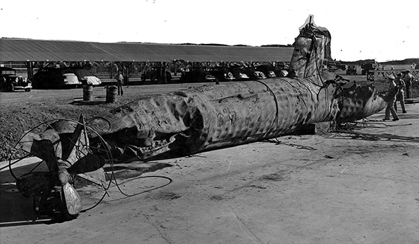 A Japanese midget submarine is salvaged and later buried in a landfill after being sunk by USS Monaghan during the Pearl Harbor attack. The sub’s hull shows the effects of depth charges and ramming. A hole visible in the after part of the conning tower may be from a five shell. The upper background had been painted over for censorship purposes. Official U.S. Navy photograph