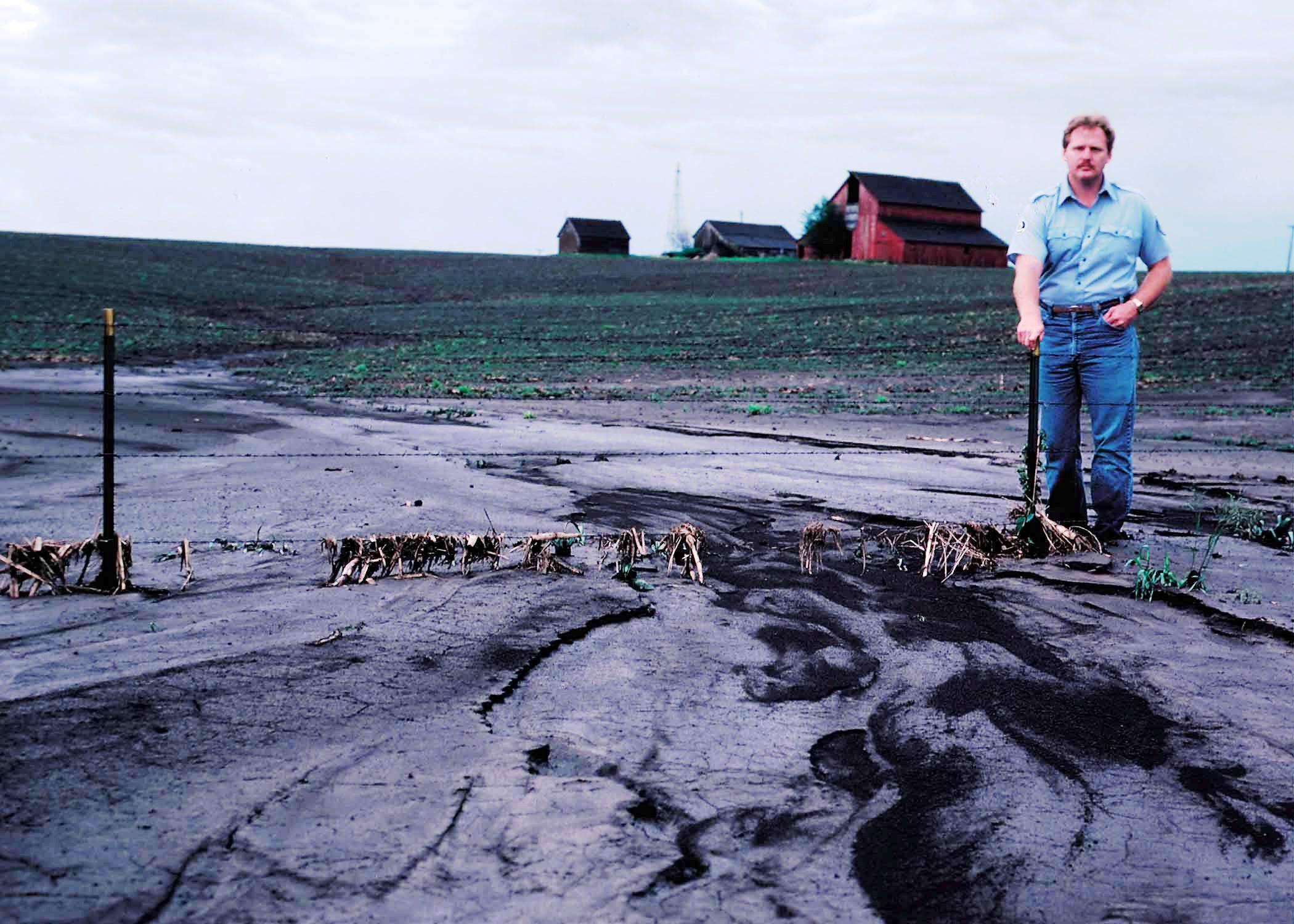Man standing near sediment coming from severely eroded crop field.