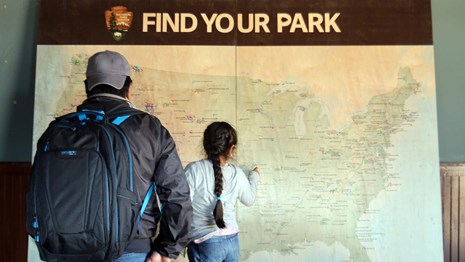 Man and girl looking at a map of the U.S. showing national parks