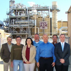 Seven people stand in front of an industrial facility with the Texas A&M logo