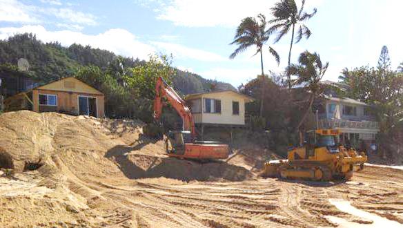 Bulldozers moving beach sand in front of houses