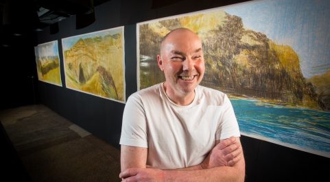 Keith Salmon smiles in front of three drawings of Hells Canyon