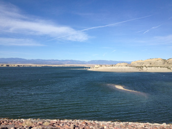 Looking west across a half full Pueblo Reservoir. Water in foreground. Mountains in background.