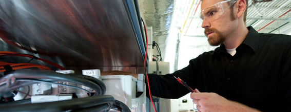 Researcher holding cables and standing in front of an open equipment chamber.