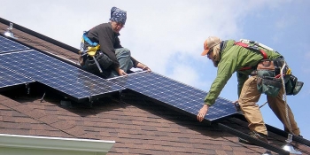 Photo of two men installing solar panels on the roof of a home.