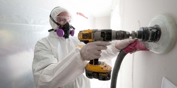 Photo of a worker in protective gear drilling a hole in the wall to install insulation.