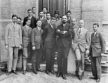 Fifteen men in suits, and one woman, pose for a group photograph