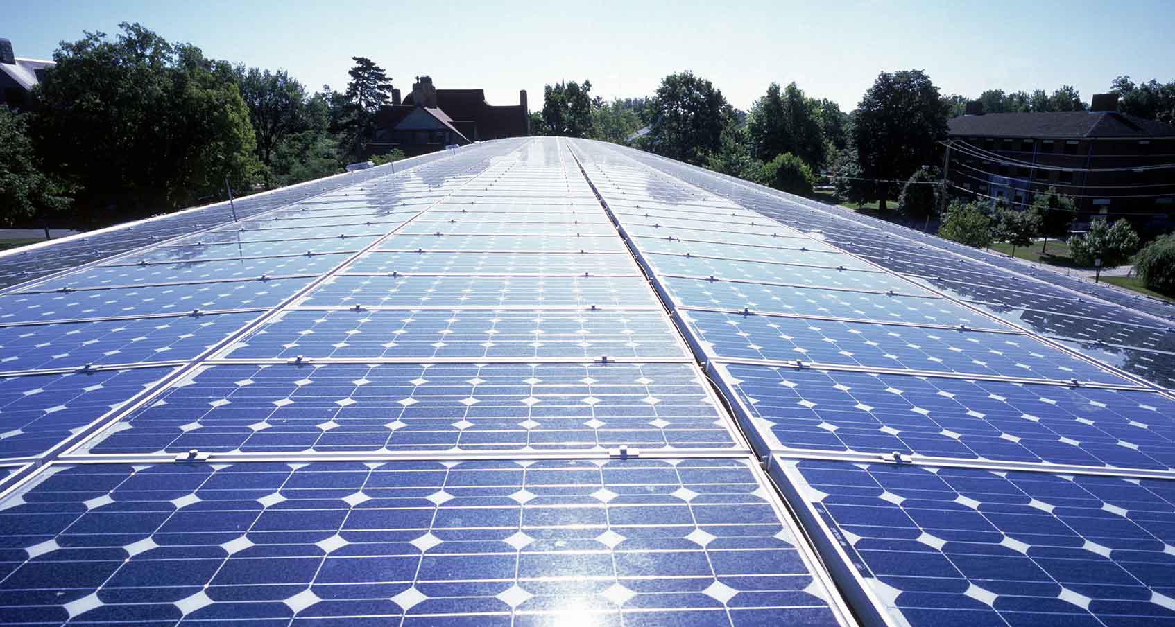 Photo of a large silicon solar array on a roof with a blue sky and trees in background.