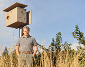 Mike Omeg standing next to an owl box on his property.