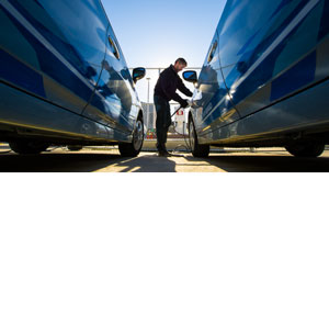 Photo of man standing between two vehicles and plugging the vehicle on the right into a charging station.