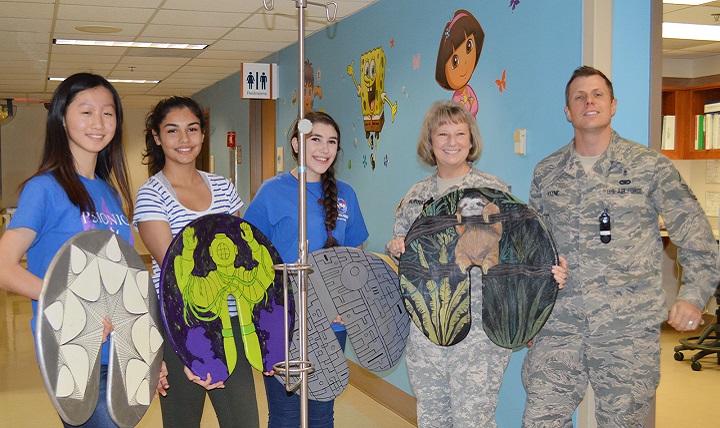 Lillian Sun, Amaya Mali and Sophie Rosenberg, students with the Westlake Robotics Club, display a few of their donated IV pole "lilypads" with the help of Army Col. Elizabeth Murray and Air Force Master Sgt. Sean Keene in an inpatient pediatric ward. The Robotics Club students constructed and donated 10 lily pads to pediatric patients at Brooke Army Medical Center. ( U.S. Army photo by Elaine Sanchez)