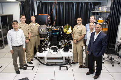 NPS students and faculty show off their recently acquired $3 million High Energy Laser Beam Control Research Testbed (HBCRT) at the university’s Department of Mechanical and Aerospace Engineering. Pictured from left to right with the HBCRT are: NPS Research Professor Jae Jun Kim, Ensign Patrick Dods, Lts. Andrew Bradstreet and Neehor Pandya, Research Associates Bautista Fernandez and Rober Van Nice and Distinguished NPS Professor Brij Agrawal. Photo courtesy of NPS.