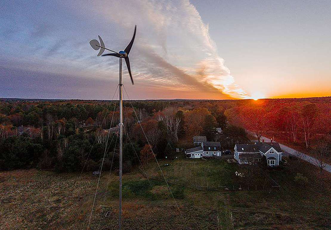 Photo of a small wind turbin in the foreground with a sunset in the background.