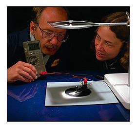 Photo of two researchers analyzing a thin, circular shaped film under a small light.