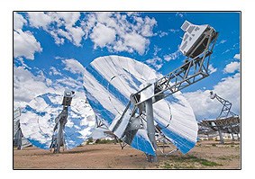 Photo of a blue and white, metallic circular mirror with a large antenna pointing toward the sky from the middle of the mirror. A blue sky with clouds are displayed in the background of the photo.