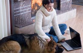 Woman sitting in front of fireplace with dog and laptop