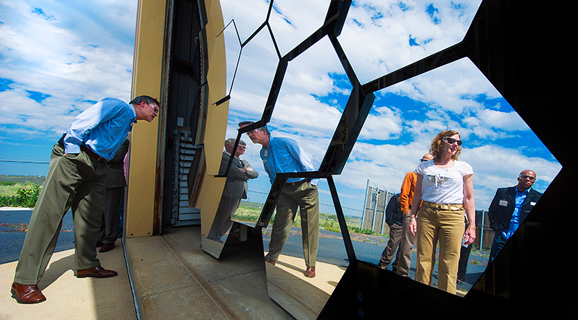 Photo of large hexagonal mirrors—part of the High-Flux Solar Furnace—reflecting images of people looking at it