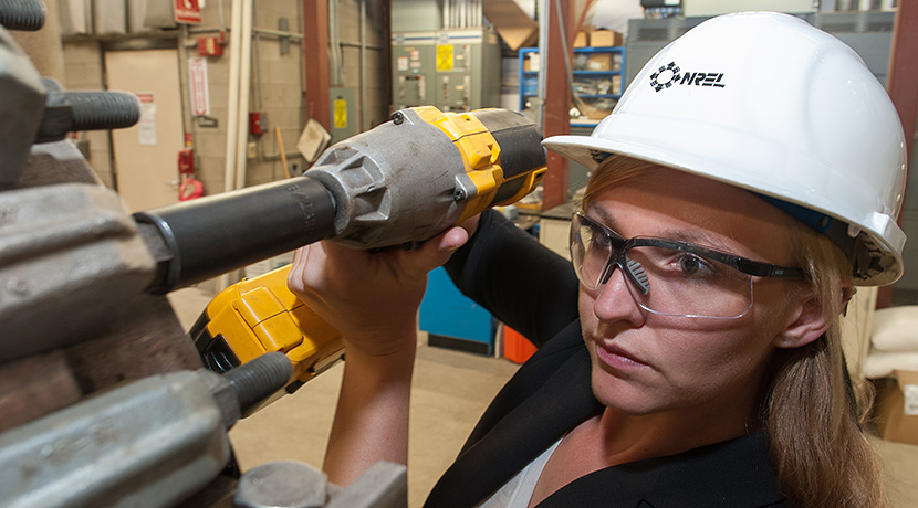 Photo of a woman in a hard hat and safety glasses using a drill to loosen a bolt on reactor equipment