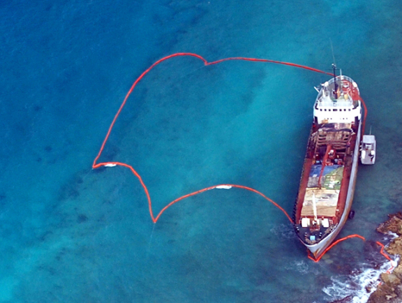 A ship run aground on coral reef in Puerto Rico is surrounded by protective oil boom.